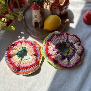 Peut inclure: Deux chouchous faits à la main au crochet, aux couleurs vives. L'un présente un mélange de rouge, rose, orange et vert. L'autre a des teintes violettes, jaunes et bleues. Ces accessoires sont parfaits pour ajouter une touche de couleur à toute coiffure.
