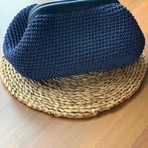 May include: A dark blue crocheted clutch purse with a black zipper.
