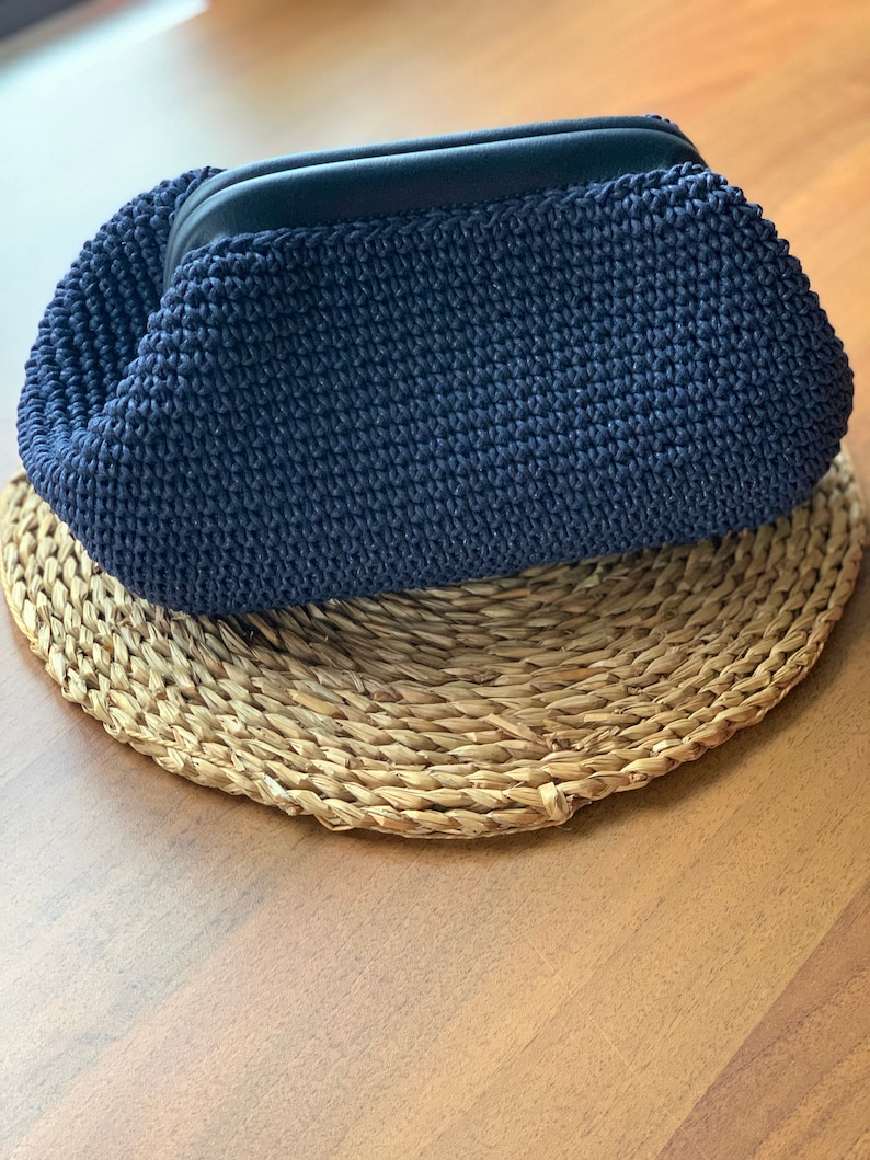 May include: A dark blue crocheted clutch purse with a black zipper.
