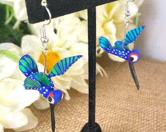 May include: A pair of blue and green hummingbird earrings with silver hooks. The hummingbirds have white dots and red eyes.