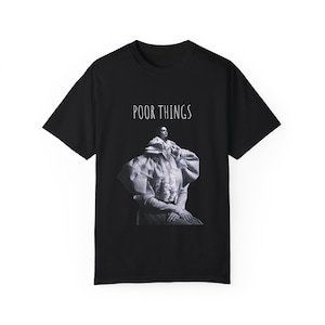May include: Black t-shirt with a graphic print of a woman wearing a white ruffled blouse and the text "POOR THINGS" in white.
