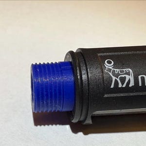 Könnte beinhalten: Nahaufnahme eines schwarzen Objekts mit einem blauen Gewindeende. Das Objekt trägt das Wort "novo" und ein Kuhlogo. Der Hintergrund ist eine schlichte weiße Oberfläche.