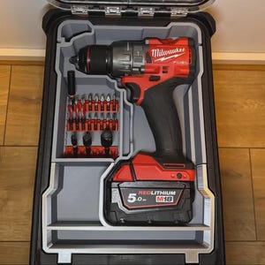 Könnte beinhalten: Ein roter und schwarzer Milwaukee FUEL Bohrer und Bit-Set in einem schwarzen Koffer. Der Bohrer hat einen schwarzen Griff und einen roten Körper mit dem Milwaukee-Logo. Der Koffer enthält verschiedene Bohrer und Zubehör.