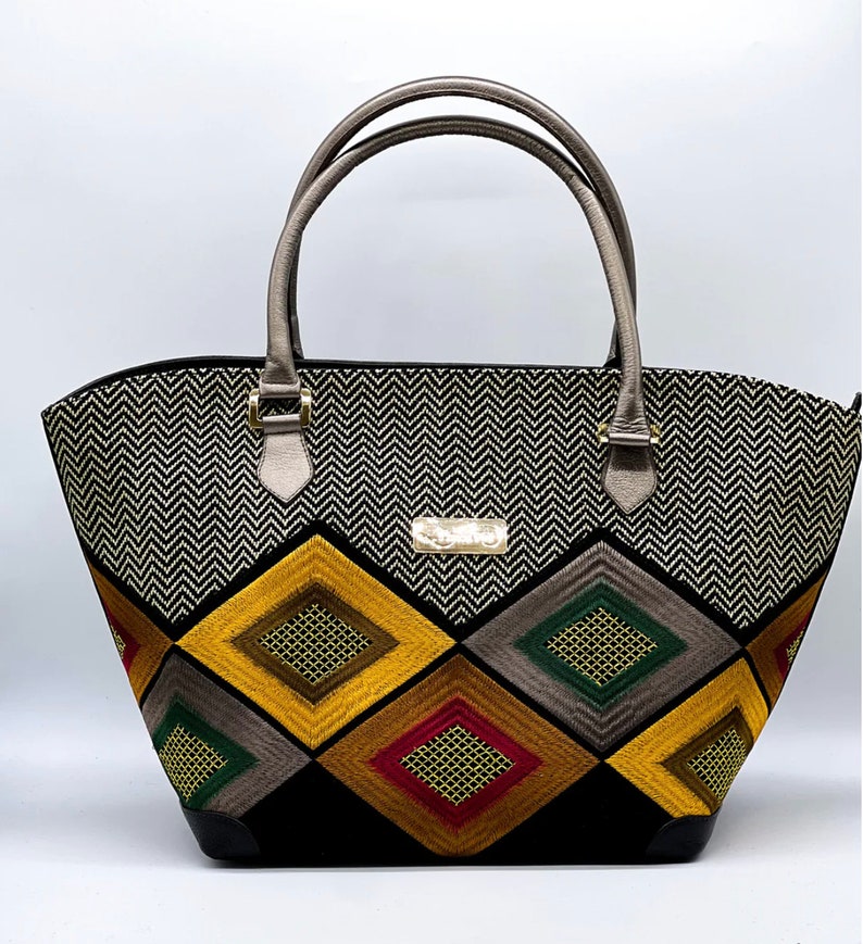May include: A black and white chevron patterned tote bag with a geometric design of colorful embroidered diamonds. The bag has two brown leather handles.