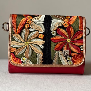 May include: A red leather crossbody bag with an embroidered floral design on the flap. The embroidery features orange, green, and white flowers. The bag has gold-tone metal trim and hardware.