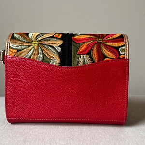 May include: A red rectangular handbag with a floral embroidered flap. The flap features colourful embroidered flowers in shades of orange, yellow, and green. The bag has a gold-coloured clasp.