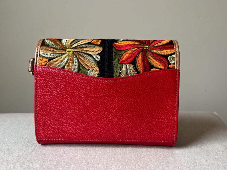 May include: A red rectangular handbag with a floral embroidered flap. The flap features colourful embroidered flowers in shades of orange, yellow, and green. The bag has a gold-coloured clasp.
