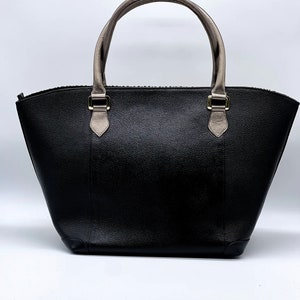 May include: A black leather tote bag with a zipper closure and two top handles. The handles are made of a light brown leather. The bag has a slightly rounded shape.
