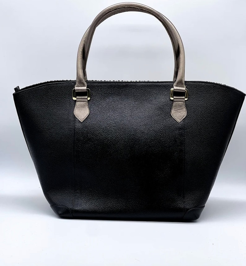 May include: A black leather tote bag with a zipper closure and two top handles. The handles are made of a light brown leather. The bag has a slightly rounded shape.