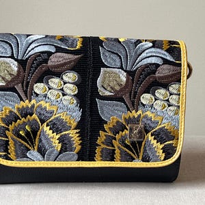 May include: Black clutch with embroidered floral design in yellow, gray, and brown. The bag has a yellow trim and a silver-colored metal clasp. The floral pattern is detailed and covers the front of the bag.