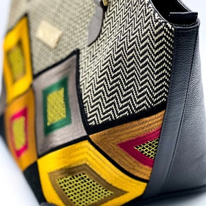 May include: A large tote bag with a geometric pattern of yellow, red, green, and brown fabric. The bag has a black leather bottom and a zipper closure.