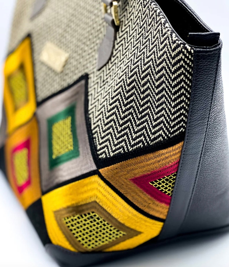 May include: A large tote bag with a geometric pattern of yellow, red, green, and brown fabric. The bag has a black leather bottom and a zipper closure.
