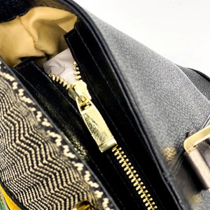 May include: A black leather handbag with a gold zipper and a woven fabric detail. The bag has a top handle and a gold buckle.
