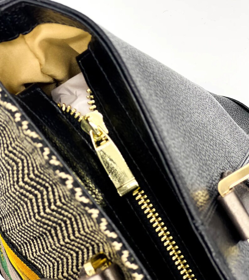 May include: A black leather handbag with a gold zipper and a woven fabric detail. The bag has a top handle and a gold buckle.