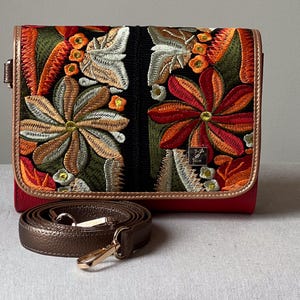 May include: A red handbag with a floral embroidered design in shades of orange, green, and brown. The bag has a brown leather strap and gold-coloured hardware. The flap closure is outlined in brown leather.