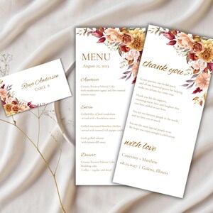 May include: Wedding stationery set featuring a menu, thank you card, and place card. The cards have a floral design in shades of orange, burgundy, and gold. The menu lists appetizers, entrees, and dessert.