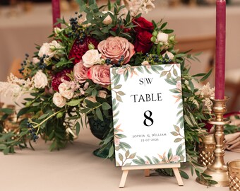 Pode incluir: Um cartão de número de mesa branco com um design floral e o texto "S/W Table 8 Sophia & William 23-07-2023". O cartão está em um pequeno cavalete de madeira.