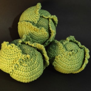 Op de afbeelding: Drie gehaakte koolkoppen in tinten groen. De koolkoppen zijn gemaakt van een getextureerd garen en hebben een realistisch uiterlijk.