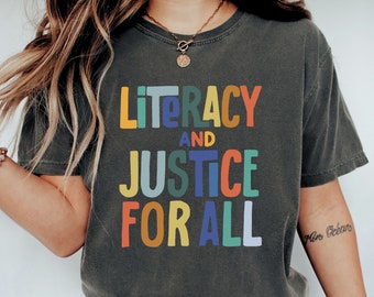 May include: A dark grey t-shirt with the text "Literacy and Justice for All" in colourful letters. The letters are in a rainbow colour scheme.