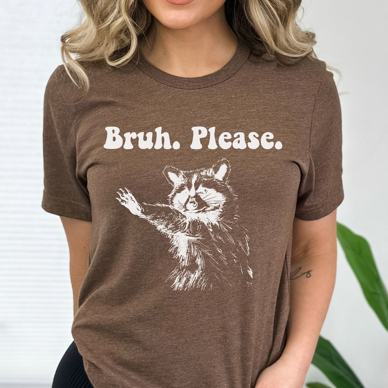 May include: A brown t-shirt featuring the text "Bruh. Please." and a white illustration of a raccoon with its paw outstretched.