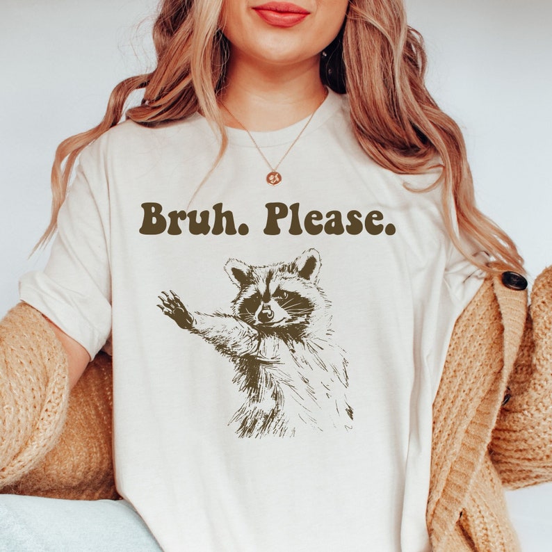 May include: White t-shirt featuring a brown raccoon graphic and the text "Bruh. Please."