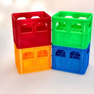 Könnte beinhalten: Vier übereinander gestapelte Plastikkisten zur Aufbewahrung von Batterien. Die oberste Kiste ist grün und trägt die Aufschrift "AA Batterien". Die nächste Kiste ist blau und trägt die Aufschrift "AAA Batterien". Die nächste Kiste ist gelb und trägt die Aufschrift "9V Batterien". Die unterste Kiste ist rot.