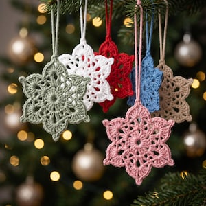 Puede incluir: Un conjunto de seis adornos de copos de nieve tejidos a ganchillo en verde salvia, blanco, rojo, azul ceniza, beige y rosa empolvado. Cada adorno en forma de estrella presenta un tejido intrincado y una cuerda a juego para colgar.