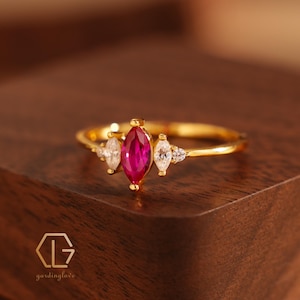 May include: A gold ring featuring a large, marquise-shaped ruby gemstone surrounded by smaller, pear-shaped white gemstones.