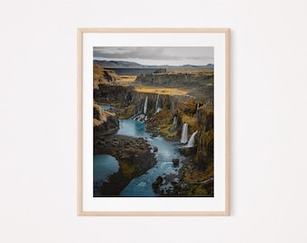 May include: A scenic aerial view of a river flowing through a rocky canyon with multiple waterfalls cascading down the cliffs. The landscape is a mix of green vegetation, brown rocks, and a blue sky with clouds.