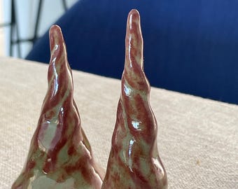 May include: Two cone-shaped ceramic sculptures with a glossy finish. The objects feature a swirling, marbled pattern of earthy sage green and deep reddish-brown glaze, tapering to a point at the top with a wide, circular base for stability.