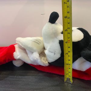 May include: A plush toy shaped like a cartoon character, featuring a black and white head, white gloves, and a red stocking. The toy measures approximately 6 inches in height.