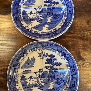 May include: Two blue and white divided plates with a classic Willow pattern. Each plate features a central section and three compartments, with a detailed landscape design. The plates are made of ceramic and have a decorative border.