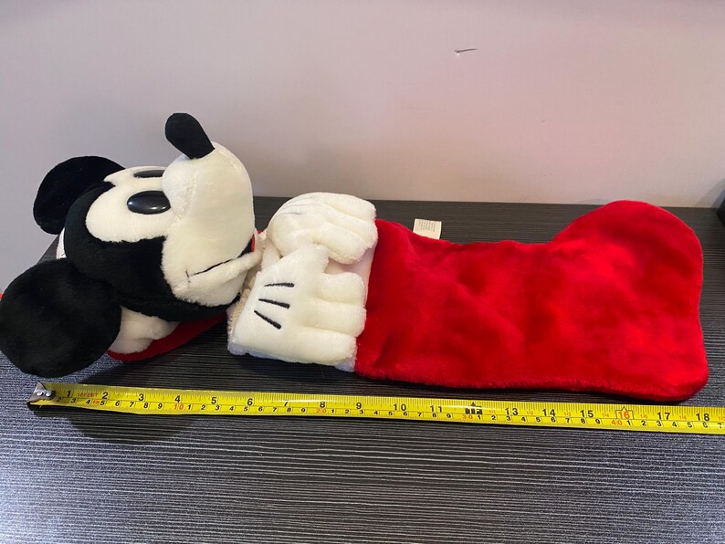 May include: A plush Mickey Mouse Christmas stocking. The stocking is red with a white cuff and Mickey's white gloved hand. Mickey's head is black and white. The stocking measures approximately 18 inches long.