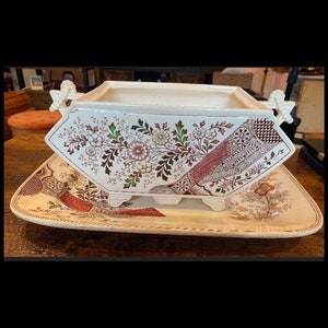 May include: A vintage ceramic serving dish and matching tray. The dish is rectangular with floral and geometric patterns in brown, red, and green on a cream background. The tray has a similar design.