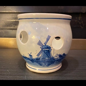 May include: White ceramic garlic keeper with two circular holes and a blue windmill design. The Dutch-style container features a blue rim and base, with a detailed illustration of windmills and a village scene.
