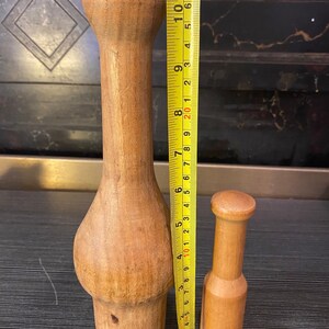 Peut inclure: Deux ustensiles de cuisine en bois. Le plus grand mesure environ 25 cm de haut, avec une section m&eacute;diane renfl&eacute;e et un sommet arrondi. Le plus petit mesure environ 13 cm de haut. Les deux sont en bois clair.