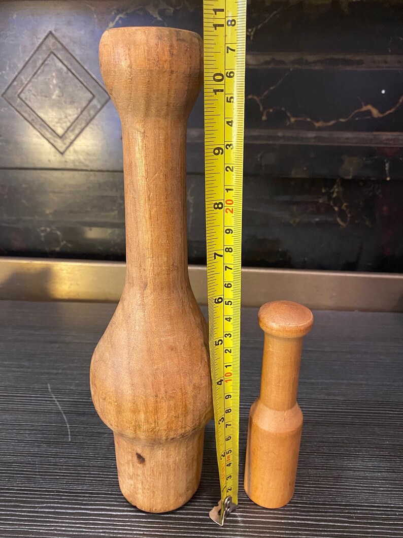 Peut inclure: Deux ustensiles de cuisine en bois. Le plus grand mesure environ 25 cm de haut, avec une section m&eacute;diane renfl&eacute;e et un sommet arrondi. Le plus petit mesure environ 13 cm de haut. Les deux sont en bois clair.