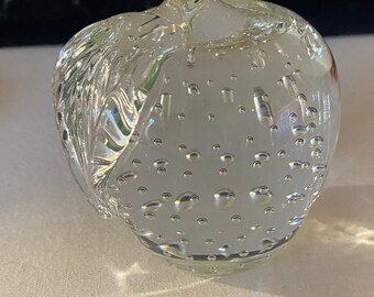 Könnte beinhalten: Ein dekoratives Objekt in Apfelform aus klarem Glas. Das Glas hat auf einer Seite eine strukturierte Oberfläche und ist mit kleinen Blasen gefüllt. Der Stiel des Apfels besteht ebenfalls aus klarem Glas.