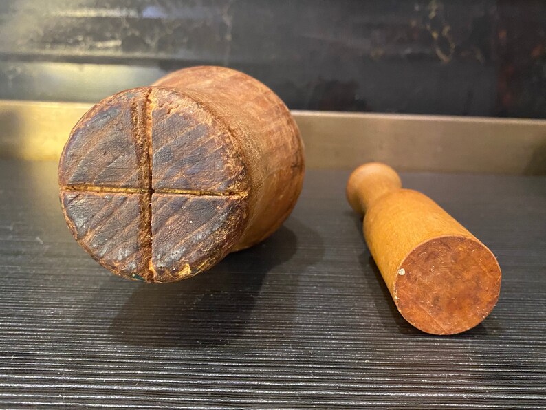 Peut inclure: Un ensemble de mortier et pilon en bois. Le mortier est de forme cylindrique avec une base en croix. Le pilon est une petite poign&eacute;e arrondie avec une base plate. Les deux pi&egrave;ces sont en bois brun clair.
