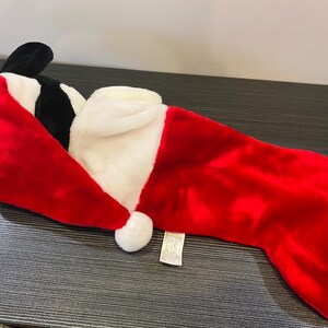 May include: A plush Christmas stocking in the shape of a character's head, featuring a red Santa hat with a white trim and a white pom-pom. The stocking is primarily red with a white cuff.