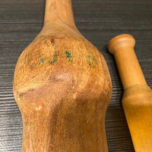 Peut inclure: Deux ustensiles de cuisine en bois. L'un est un grand pilon brun clair avec un corps bulbeux et un long manche. L'autre est un pilon cylindrique plus petit. Les deux outils ont une finition lisse et naturelle et semblent &ecirc;tre en bois dur.