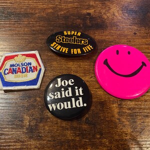 May include: A collection of four vintage pins and patches. Includes a pink smiley face button, a black button with "Joe said it would" text, a Molson Canadian Beer patch, and a Steelers pin.