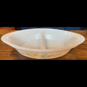 Puede incluir: Un plato de servir dividido, de forma ovalada y color blanco, con un diseño de trigo dorado. El plato tiene dos compartimentos y asas en cada extremo. Está hecho de un material duradero y es adecuado para servir alimentos.