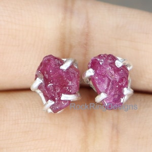 Op de afbeelding: Een paar robijn edelsteen oorstekers. Elke oorbel heeft een ruwe, dieproze robijnsteen gezet in een zilveren metalen prong setting. De oorbellen worden gepresenteerd tegen een neutrale achtergrond.