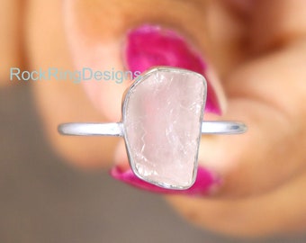 May include: A silver ring with a raw, pink rose quartz stone. The stone is a natural, irregular shape.