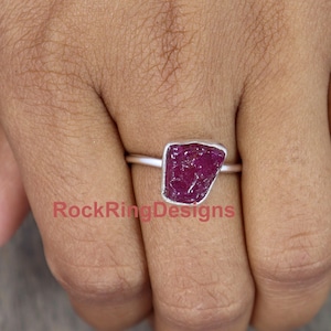 May include: A silver ring with a raw, red ruby gemstone. The ring is set on a plain silver band.