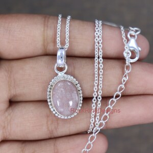 May include: A silver chain necklace with a pendant featuring a light pink oval gemstone set in a silver bezel. The pendant has a beaded edge.