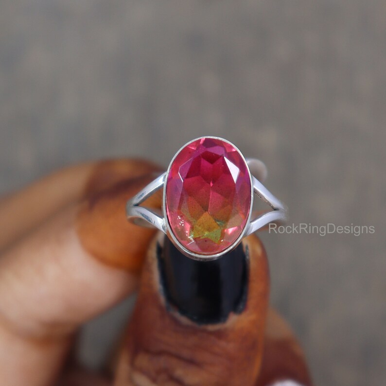 May include: A silver ring with a large oval-shaped gemstone. The gemstone is a deep red color with a slight green hue.