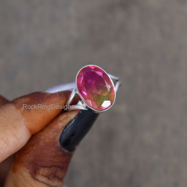 May include: A silver ring with a large oval-shaped gemstone. The gemstone is a mix of pink, green, and orange colors.