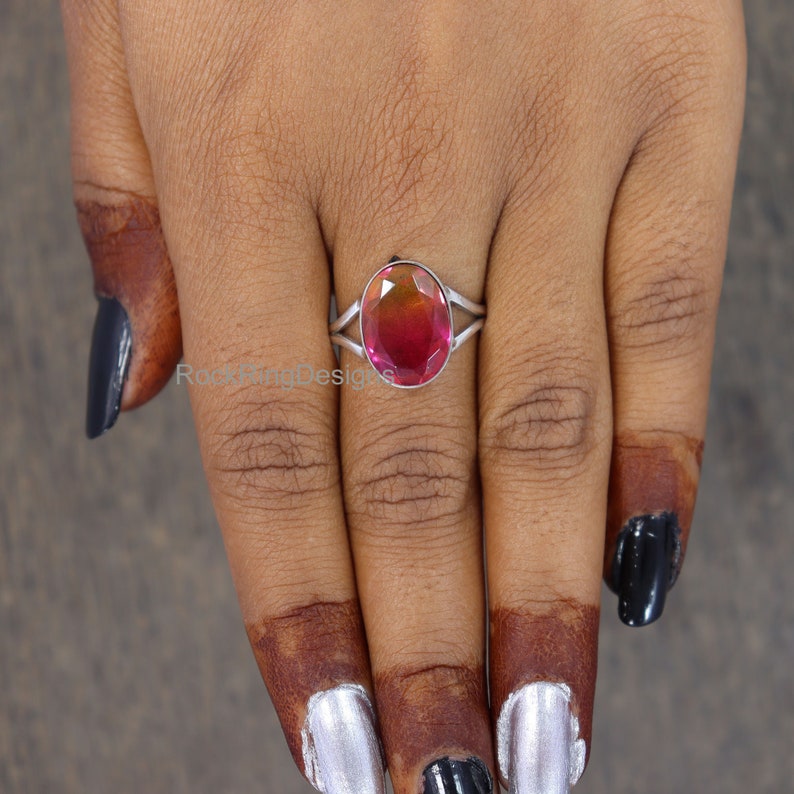 May include: A silver ring with a pink oval gemstone. The ring is on a person's finger.